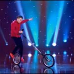 Erik Ivarsson mounting a giraffe unicycle while riding a standard unicycle