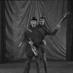 Two men dressed as devils perform a club runaround on a Pathe video